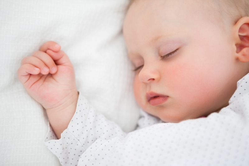 Peaceful baby lying on a bed while sleeping in a bright room